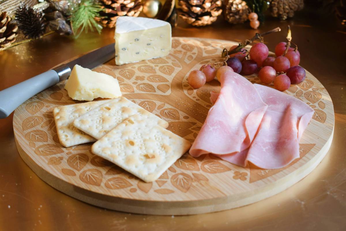 Wooden cheese serving board with lid displaying assorted cheeses and crackers on a kitchen counter